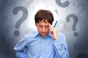 Confused person with left hand palm on left temple head with a background of question marks