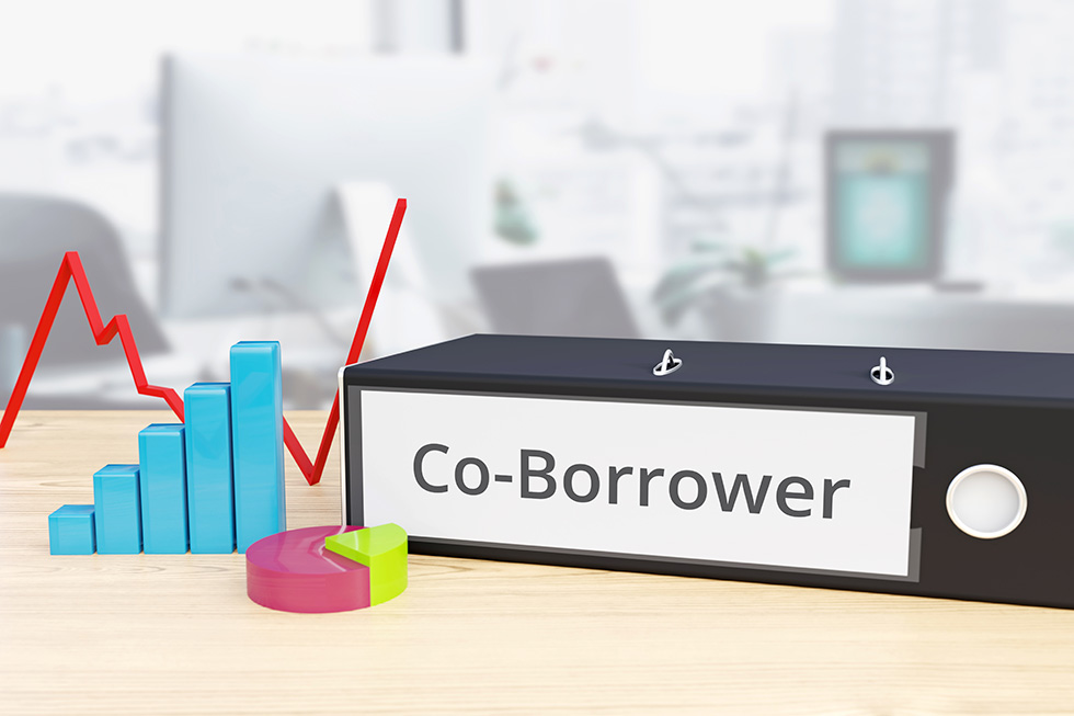 The words "Co-Borrower" is displayed on a sign that is sitting on a desk. Around it are bar charts and line graphs.