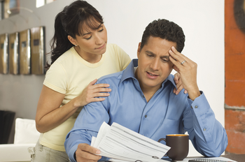 Stressed man looking at papers in hand beside a woman consoling him
