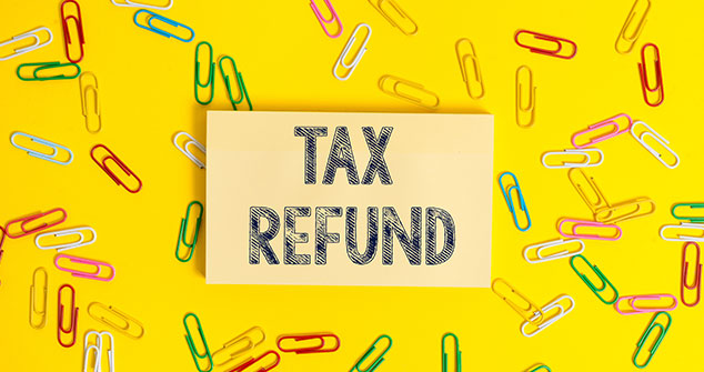 The words "Tax Refund" in capital letters are written on a yellow rectangular card. Surrounding are multi-colored paper clips, on a yellow background. The paper clips are yellow, red, green, white and blue.