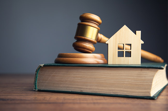Image shows a book upon Gavel to the left on the book and wood crafted home icon to the right