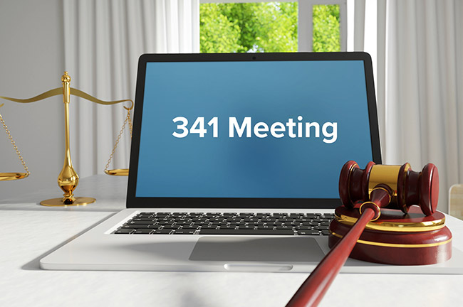 Image shows a "341 Meeting" text on the laptop screen with blue background center aligned, to the left of the laptop beam scale is placed and towards the right beside touch pad of laptop gavel is placed