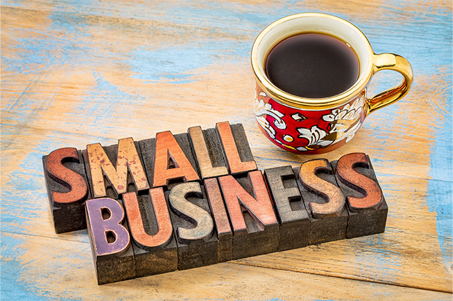 The words "Small Business" sit on a wooden table next to a red mug of coffee.