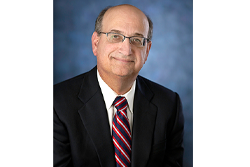 Image of attorney Bruce Levitt. He is seated and wearing a suit with a blue, white and grey striped tie. He also is wearing glasses.