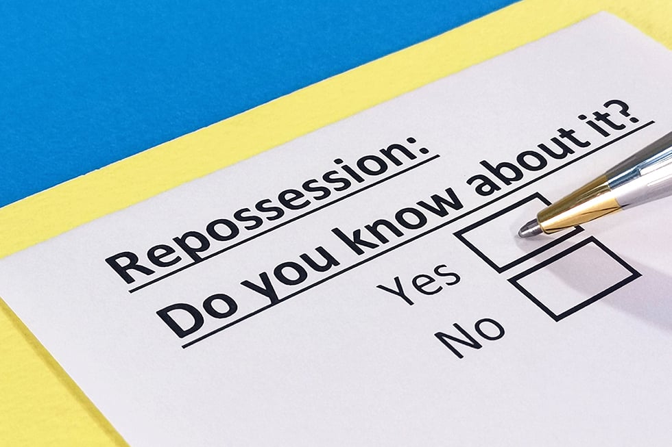 A piece of paper sits on a yellow and blue background. The paper says in typed text, "Repossession: Do you know about it?" Underneath are two boxes that say "Yes" and "No." A pen point sits in the "yes" box.