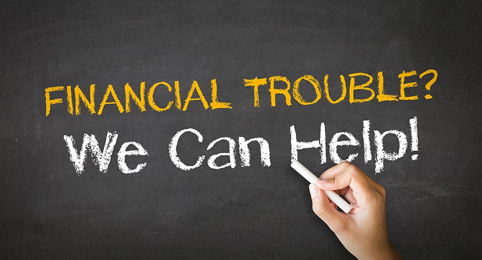 A hand is writing on a chalkboard. The chalkboard says, "Financial Trouble? We can help!"