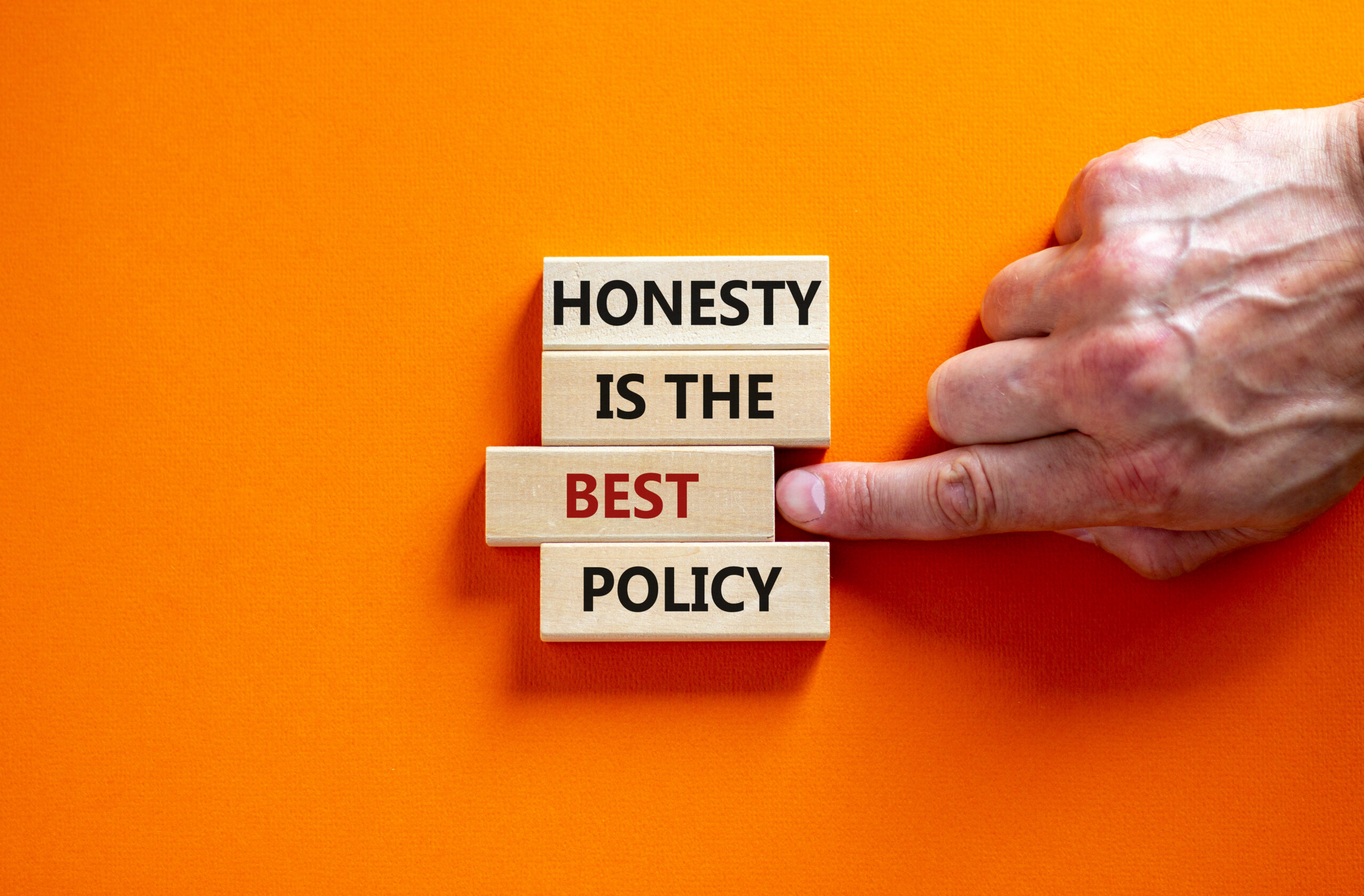 The words, "Honesty is the best policy" appear on wood blocks on an orange background. A hand on screen points to the word "best" which appears in red letters.
